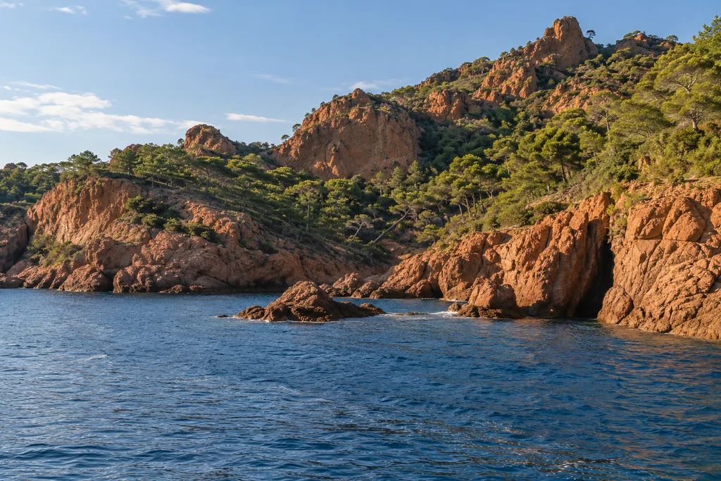 Red-rock coves and pine-covered slopes of the Estérel seen from the water in warm afternoon light
